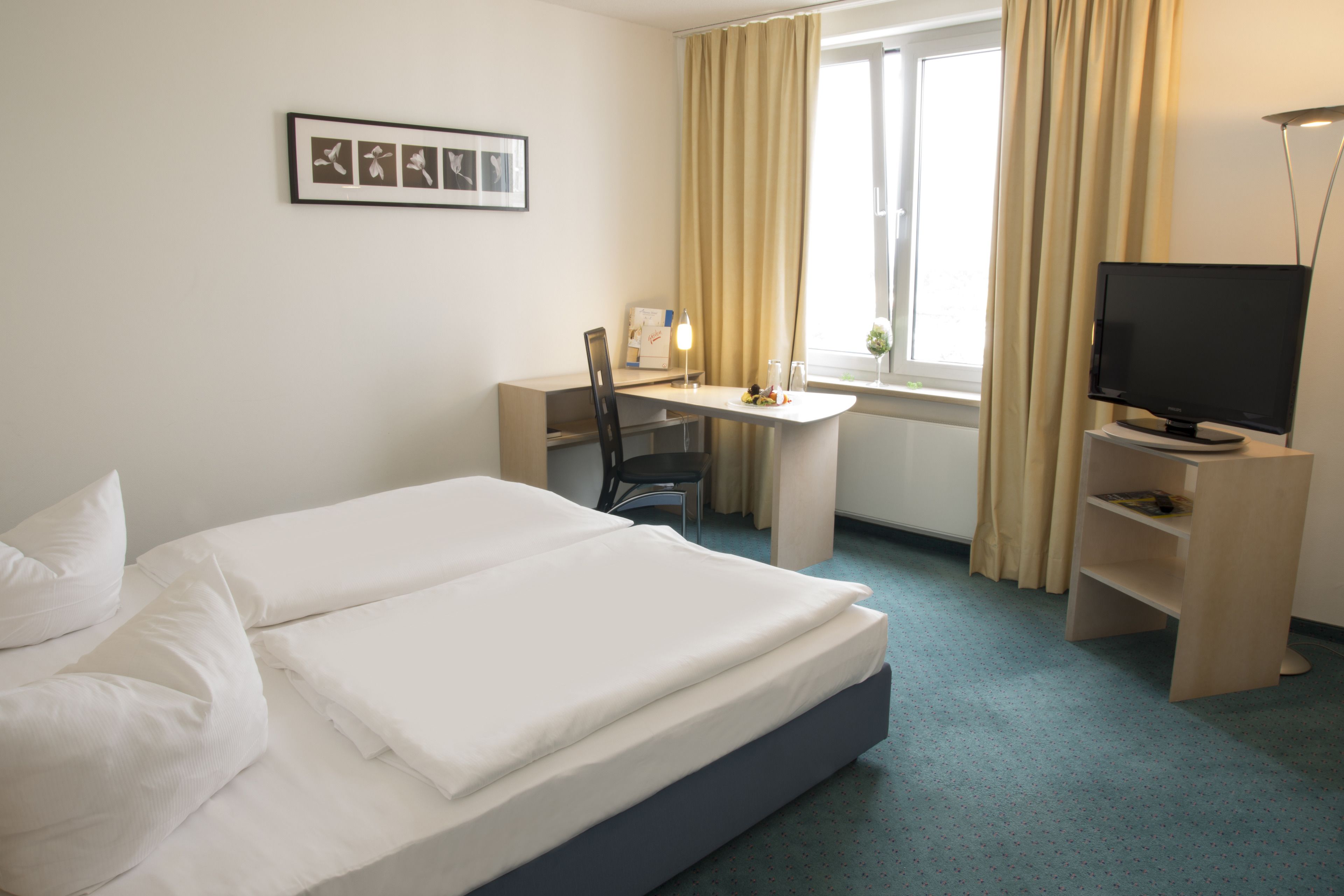 A hotel room with a bed, a desk, a chair, a television, and a window with curtains.