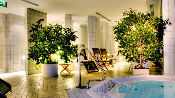 An indoor swimming pool area with tiled flooring, lounge chairs, and potted plants.