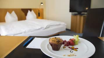 A hotel room with a neatly made bed, a dining table with a plate of food, a pen, and a notepad.