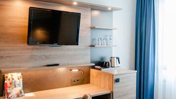 Una habitación de hotel moderna con un escritorio de madera, un televisor de pantalla plana, una silla y una cama.