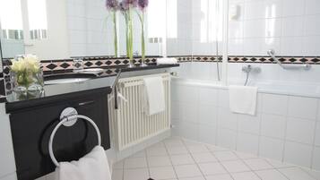 A modern bathroom with a black countertop, white tiles, a white bathtub, and a white radiator.