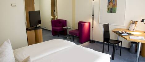 A hotel room with a bed, a desk, a chair, a television, and a painting on the wall.