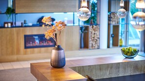 A modern reception desk with a vase of dried flowers, a bowl of green apples, and hanging pendant lights.