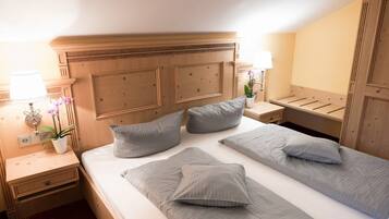 A hotel room with a wooden headboard, two beds with grey bedding, a nightstand with a lamp, a small table with a potted orchid, and a wooden wardrobe.