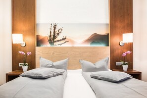 Two single beds with light grey bedding, flanked by wooden nightstands and a large framed artwork.