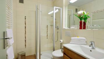 A modern bathroom with a glass-enclosed shower, a toilet, a sink with a mirror, and a small trash bin.
