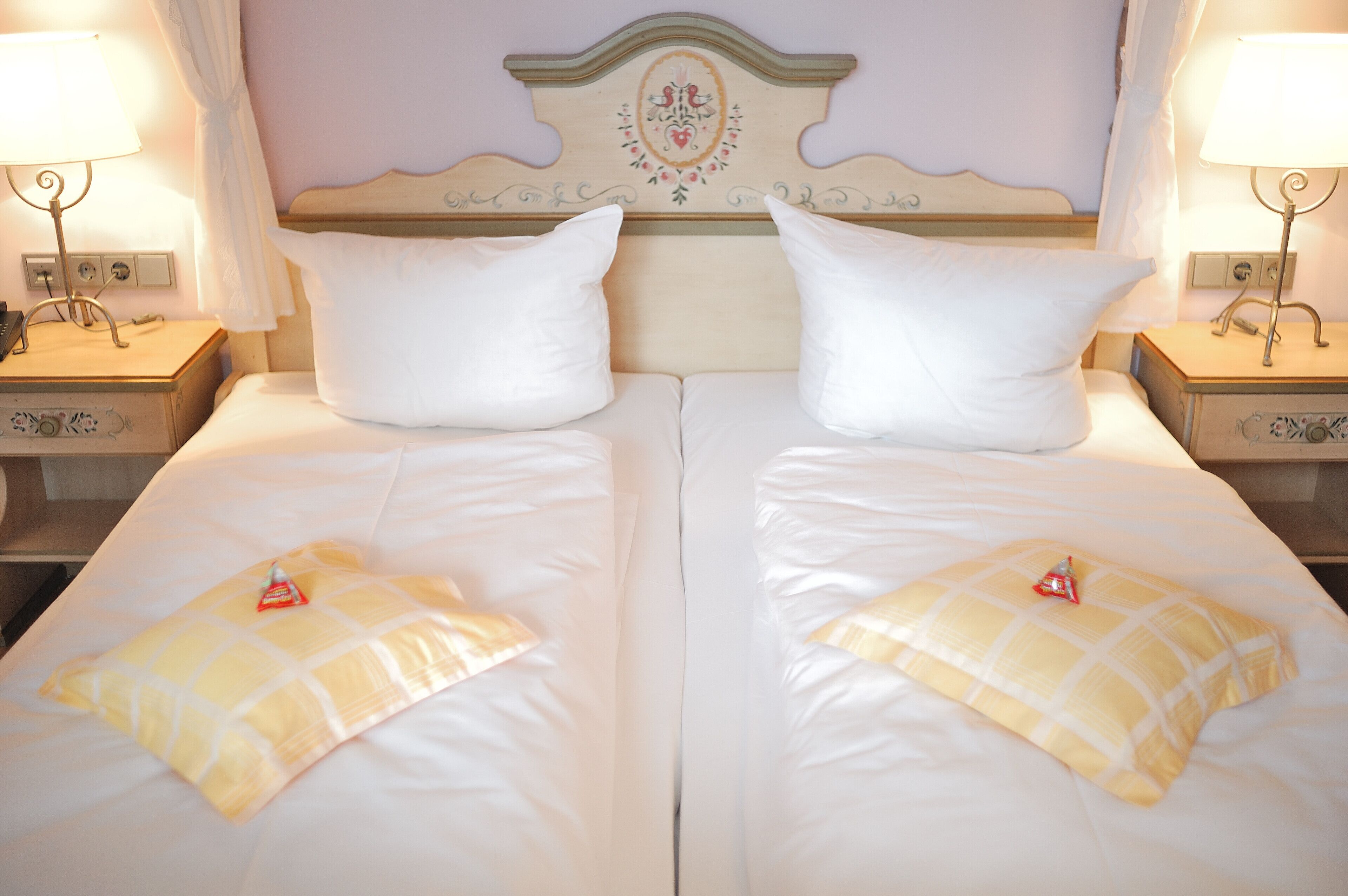 A double bed with white linens and two pillows, a decorative headboard, bedside lamps, and a small bedside table.