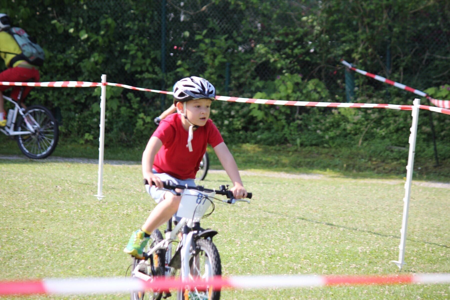 Un enfant à vélo dans un espace herbeux, avec une barrière rouge et blanche.