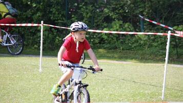 Un enfant à vélo dans un espace herbeux, avec une barrière rouge et blanche.