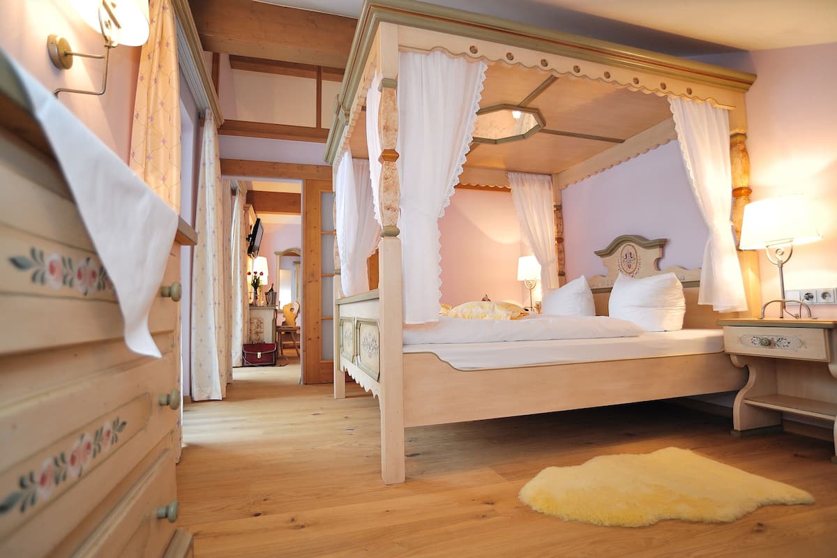 A four-poster canopy bed with white linens, a wooden dresser with floral patterns, and a small bedside table with a lamp.