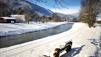 Schneebedeckte Landschaft mit Fluss, Bank und Gebäuden im Hintergrund.