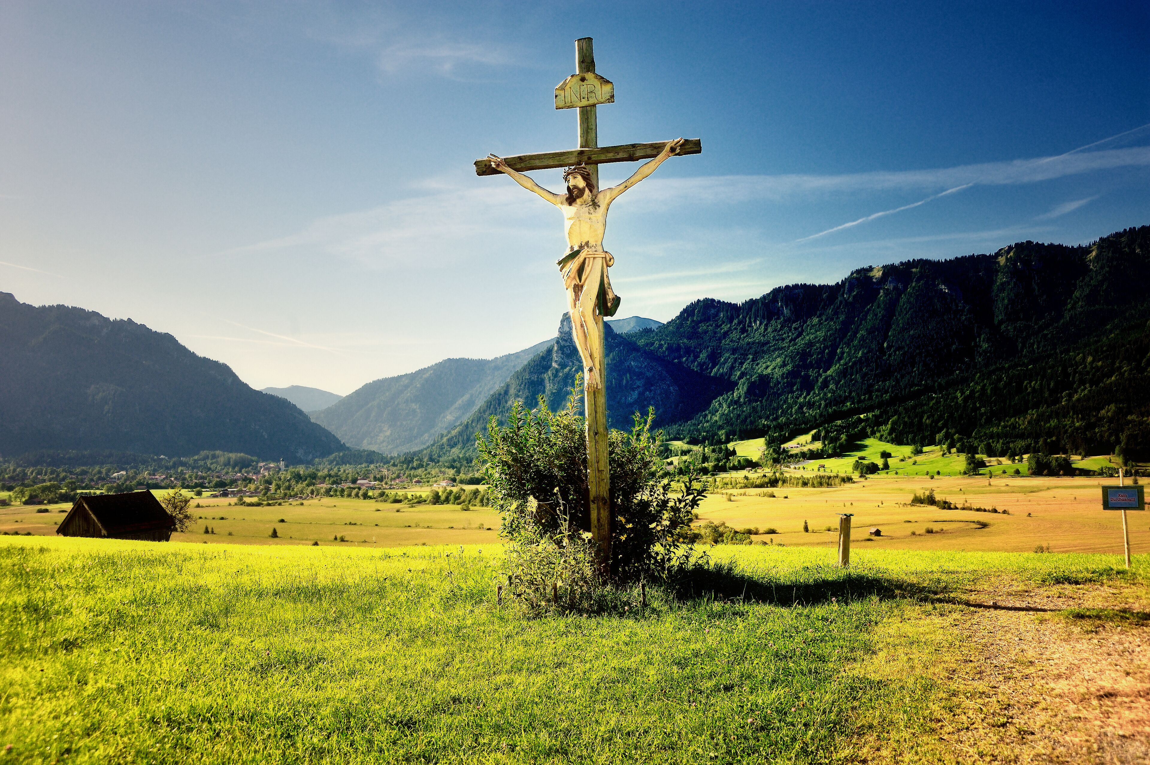 A wooden cross in a grassy field with mountains in the background.
