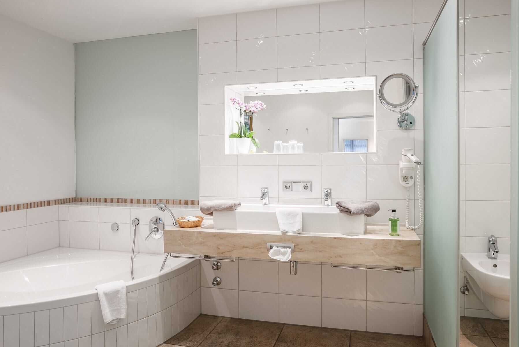 A modern bathroom with a bathtub, a sink, and a mirror. There are towels and toiletries on the counter.