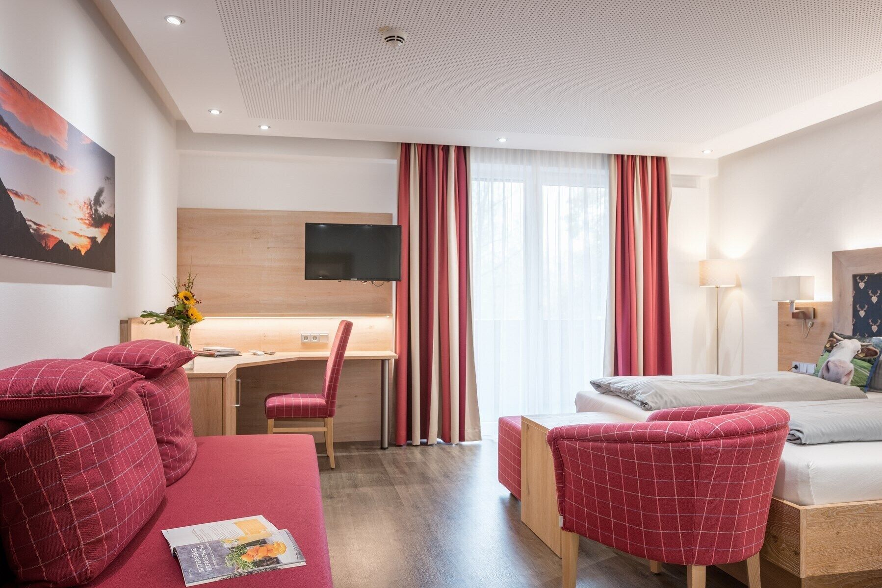A hotel room with a bed, a desk, a chair, a sofa, and a TV.