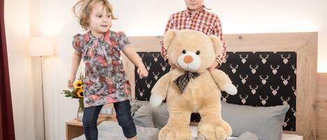 Dos niños jugando en una cama con un oso de peluche grande.
