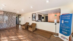 A hotel reception area with a modern design, featuring a reception desk, two armchairs, and a patterned wall. - Quality Inn Clovis (Clovis)