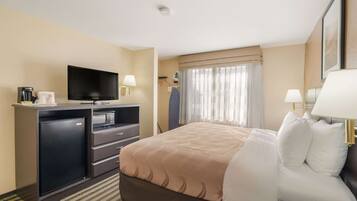 A hotel room with a bed, a TV, a desk with a computer, a coffee maker, and a refrigerator.