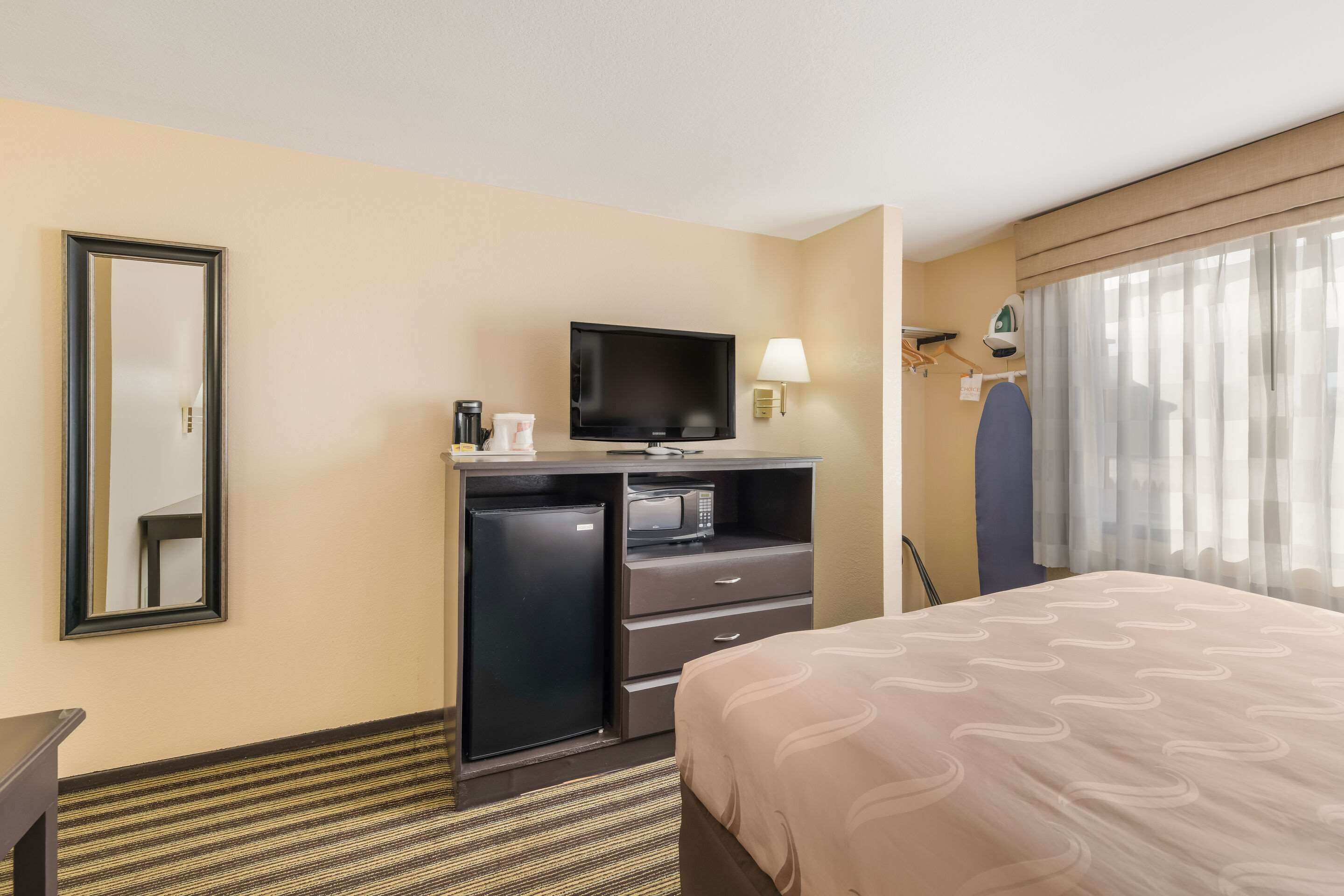A hotel room with a bed, a television, a desk with a microwave, and a mirror.