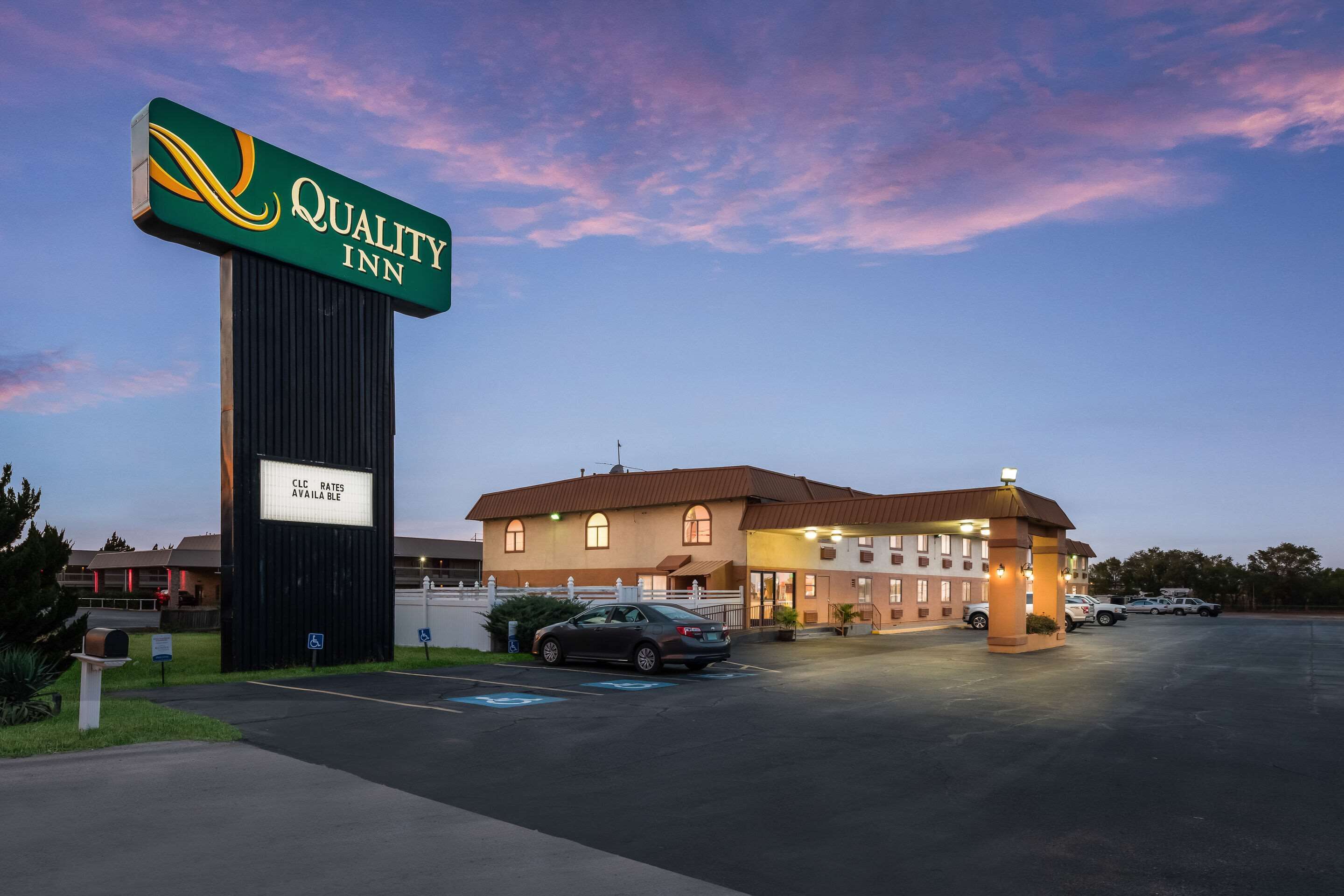 A Quality Inn with a large sign, a parking lot, and a building with a brown roof.