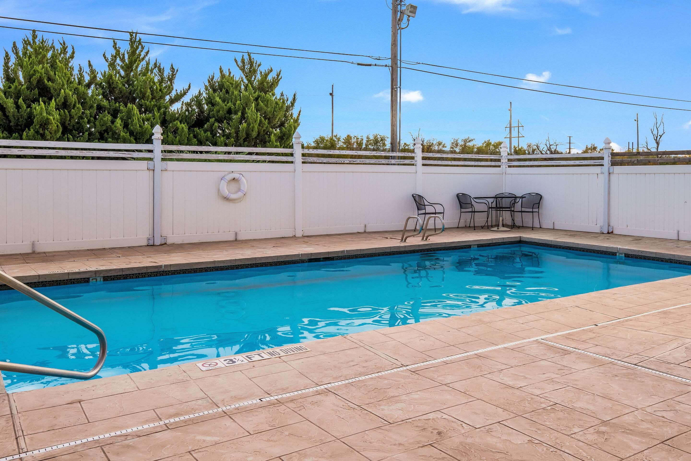 A swimming pool with a white fence, a lifeguard ring, and a seating area with chairs and a table.
