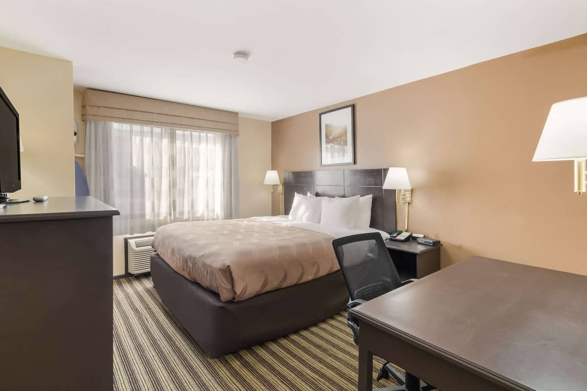 Quarto de hotel com cama grande, escrivaninha, cadeira e televisão.