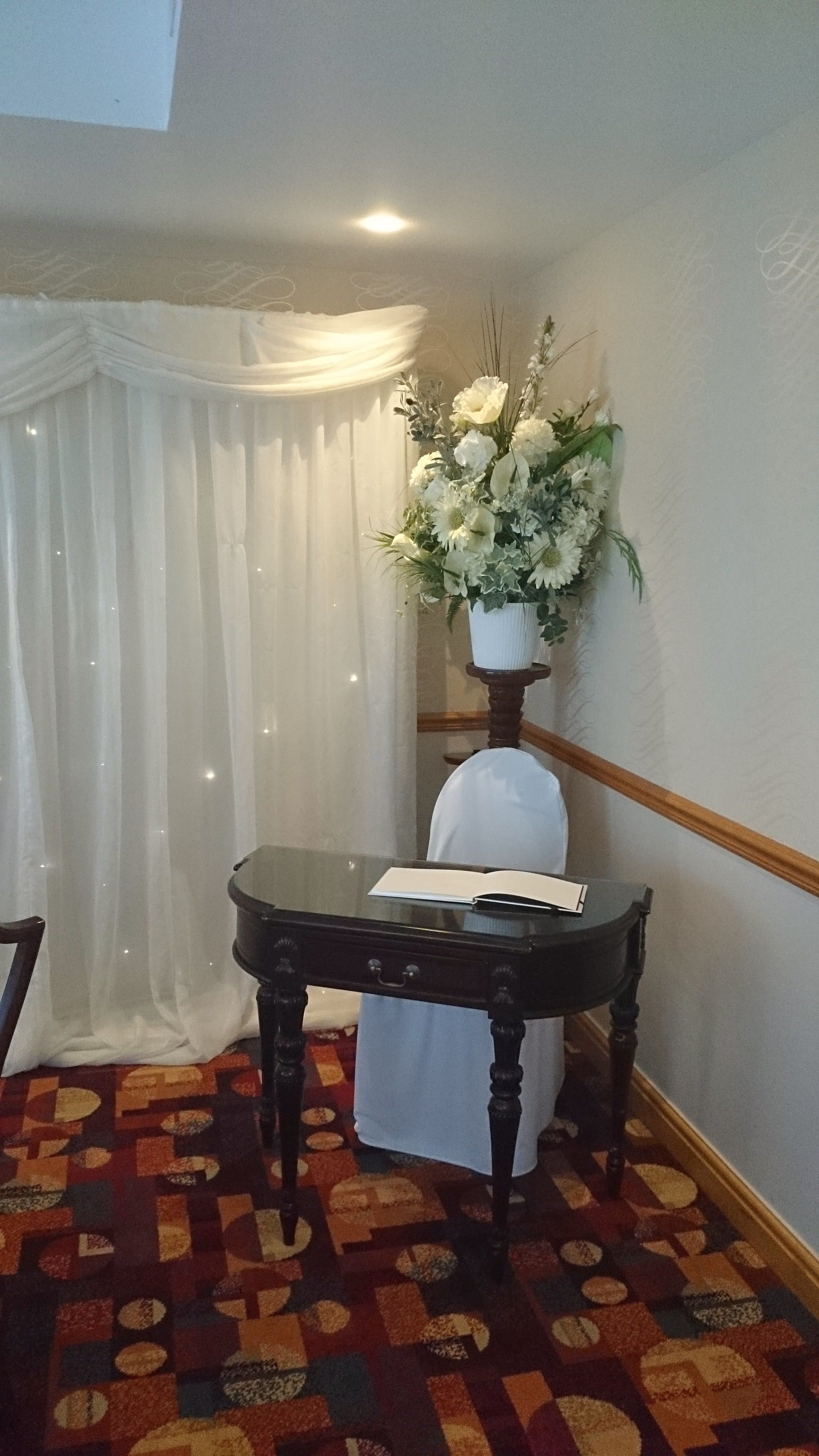 A room with a table, a chair, a white curtain, and a floral arrangement.