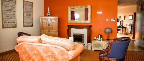 A room with an orange wall, a sofa, a chair, a fireplace, and a cabinet.