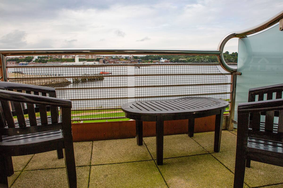 Ein Balkon mit Blick auf einen Fluss, einem Tisch und zwei Stühlen.