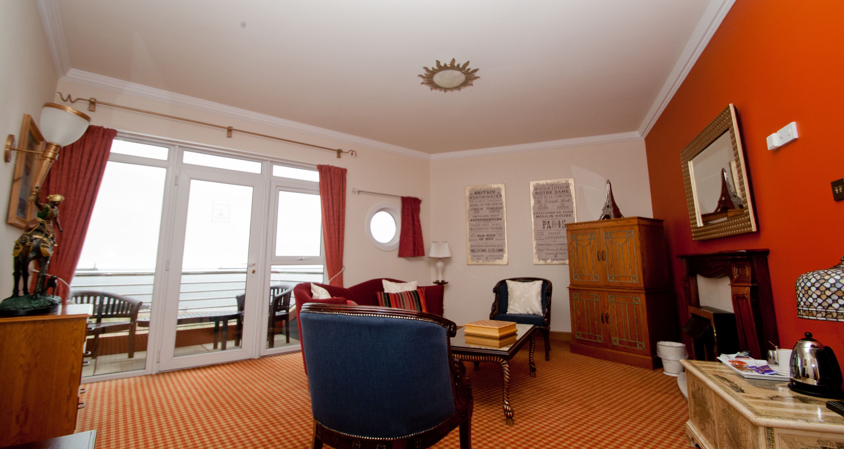 A room with a red carpet, a blue armchair, a wooden cabinet, and a table with books.