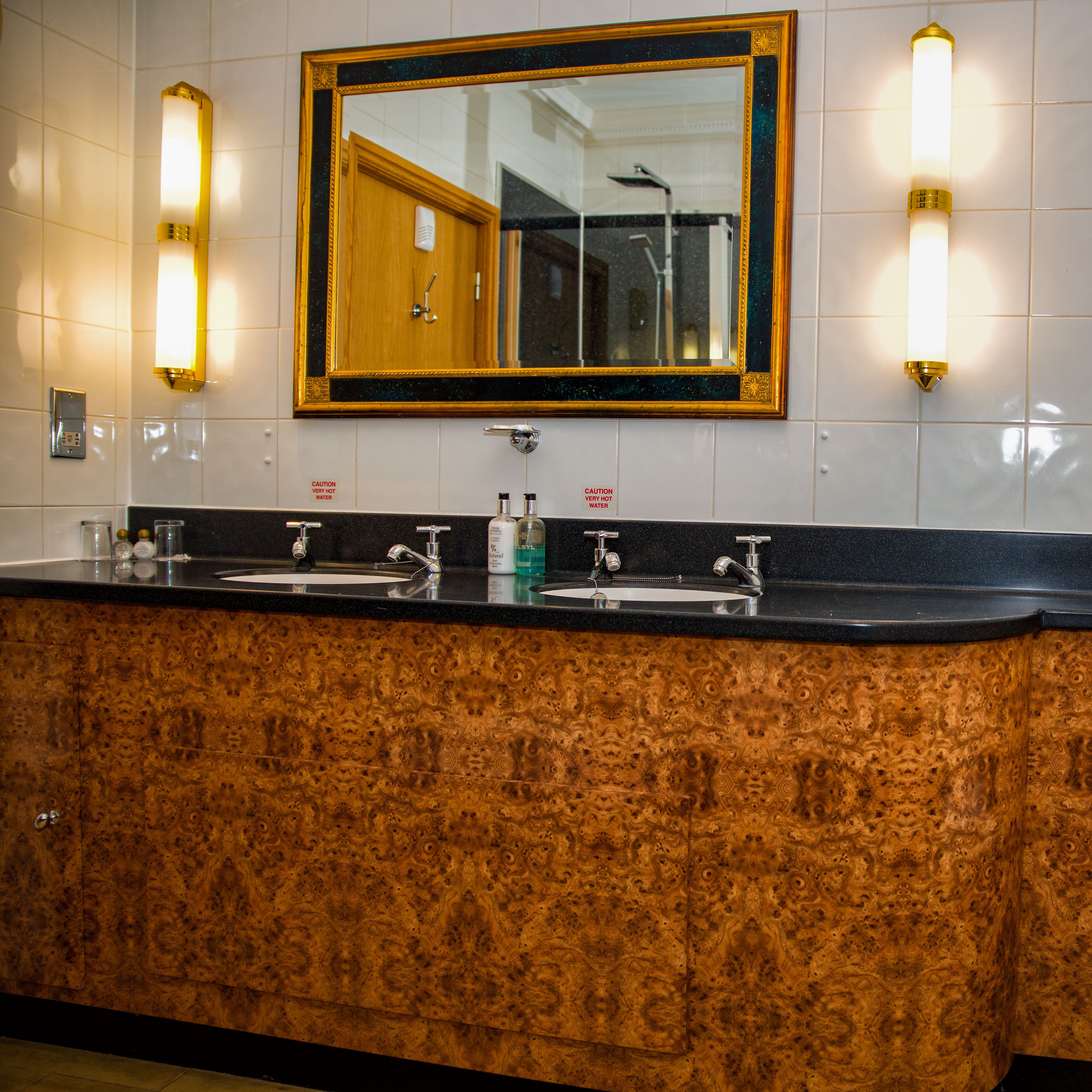 Ein Badezimmer mit einem Holzwaschtisch, zwei Waschbecken und einem großen Spiegel mit goldener Rahmung.