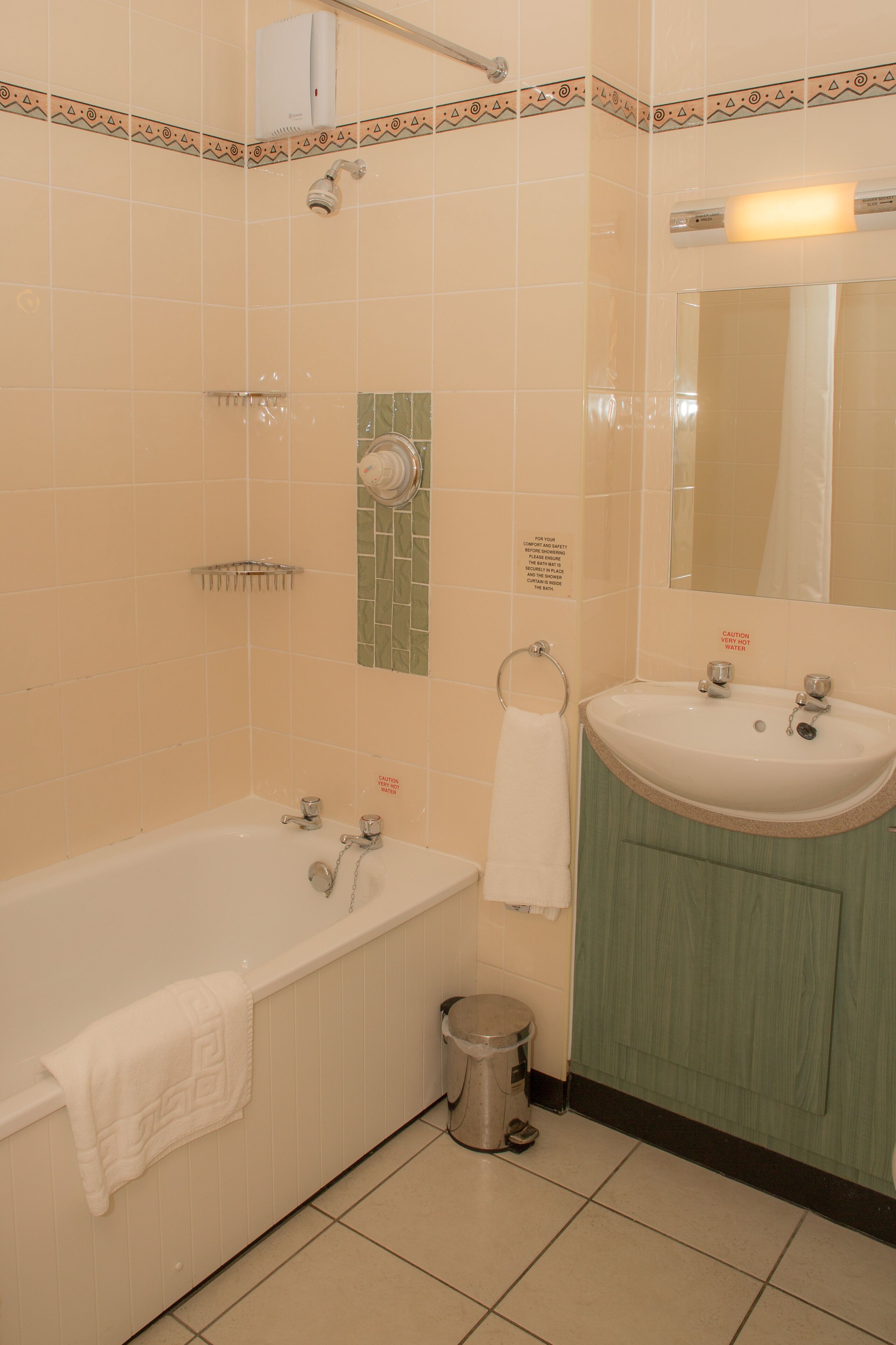 Une salle de bain avec une baignoire, un lavabo et un miroir. On y trouve également un porte-serviettes et une poubelle.