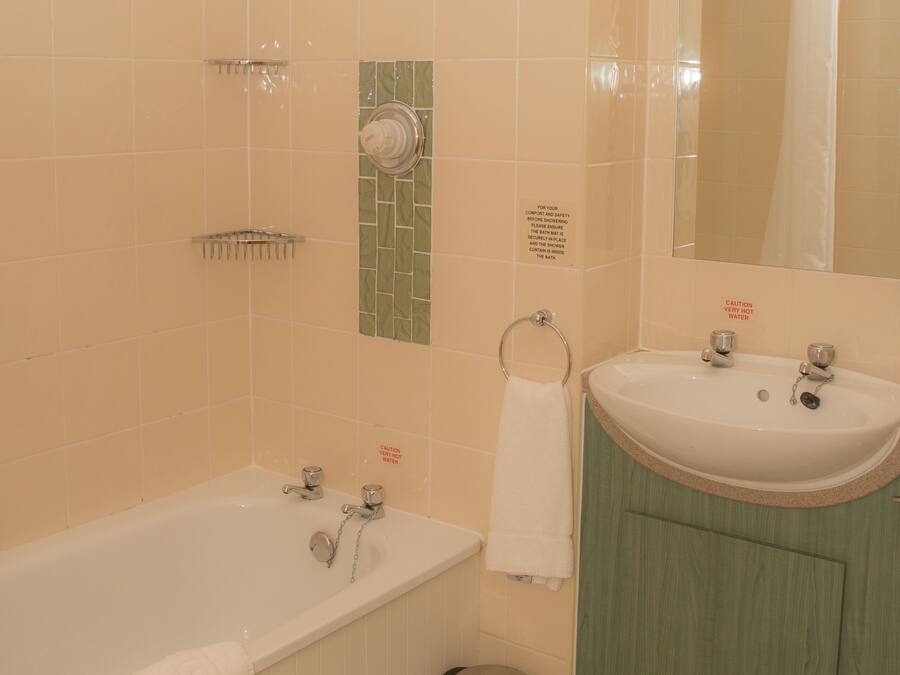Une salle de bain avec une baignoire, un lavabo et un miroir. On y trouve également un porte-serviettes et une poubelle.
