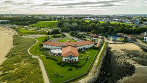 A large, circular building with a central tower, surrounded by a well-maintained lawn and a sandy beach area. - Little Haven Hotel On The Beach (South Shields)