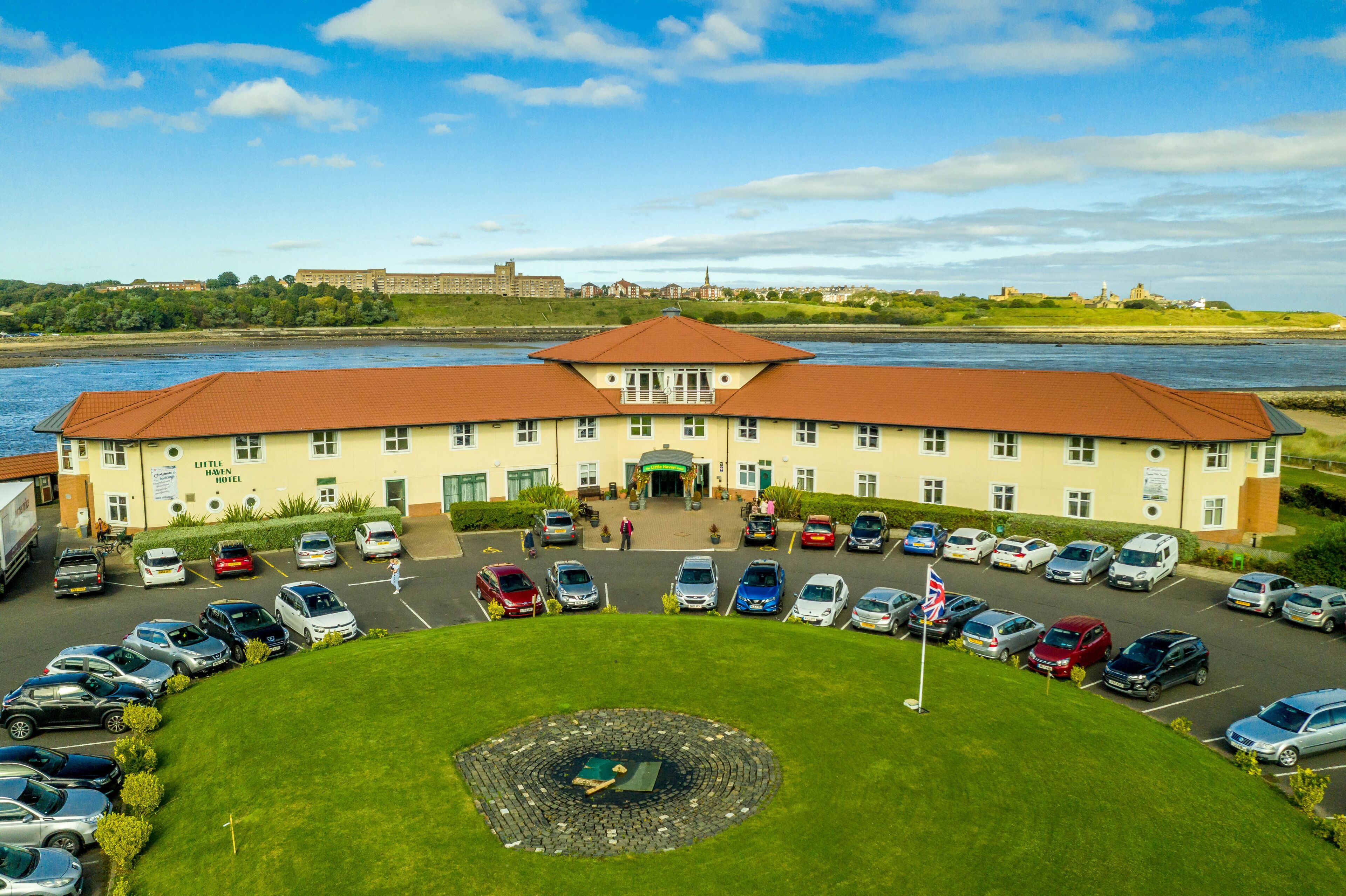 Un hotel con entrada central, estacionamiento y un río al fondo.