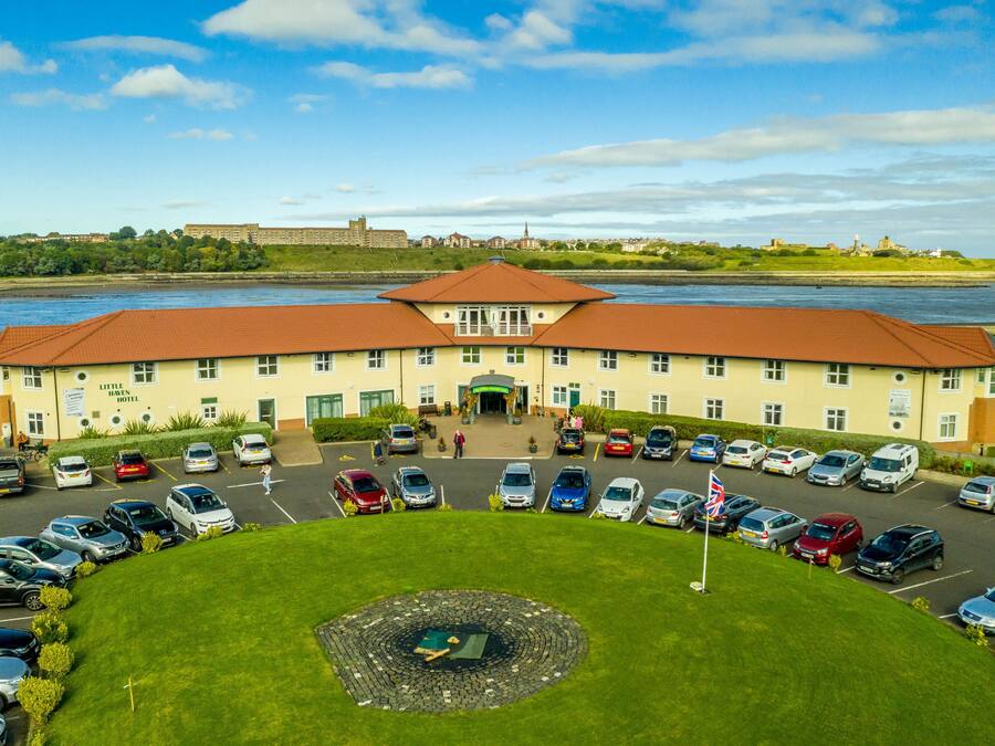 Un hotel con entrada central, estacionamiento y un río al fondo.