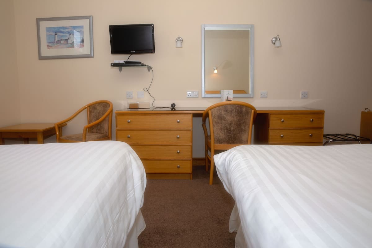 Ein Hotelzimmer mit zwei Betten, einem Schreibtisch, einem Stuhl, einem Schminktisch und einem Spiegel.