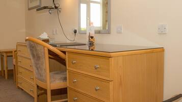 A wooden dresser with drawers, a chair, a desk, a television mounted on the wall, and a mirror above the dresser.