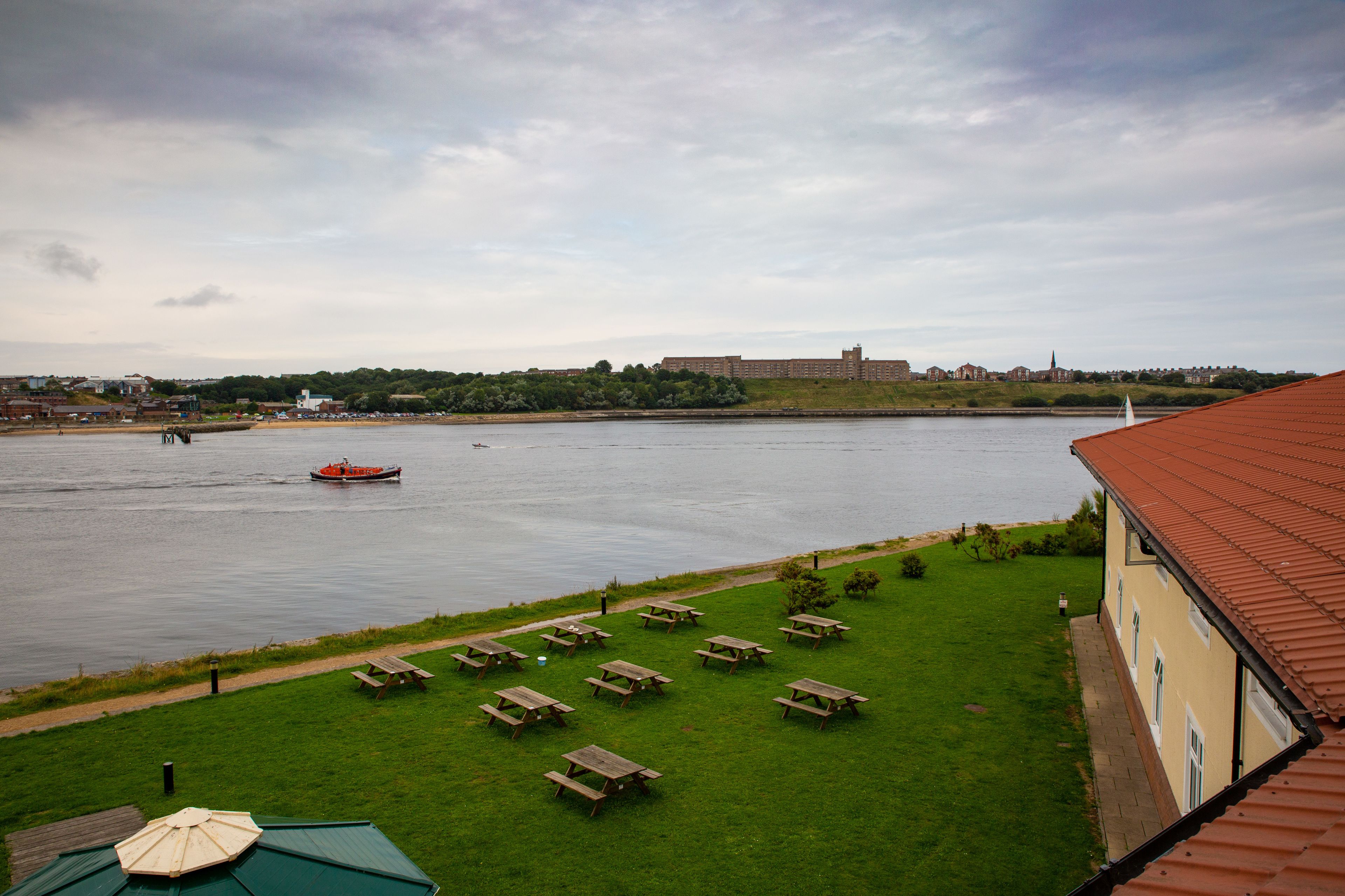 A riverside view with picnic tables and a boat on the water.