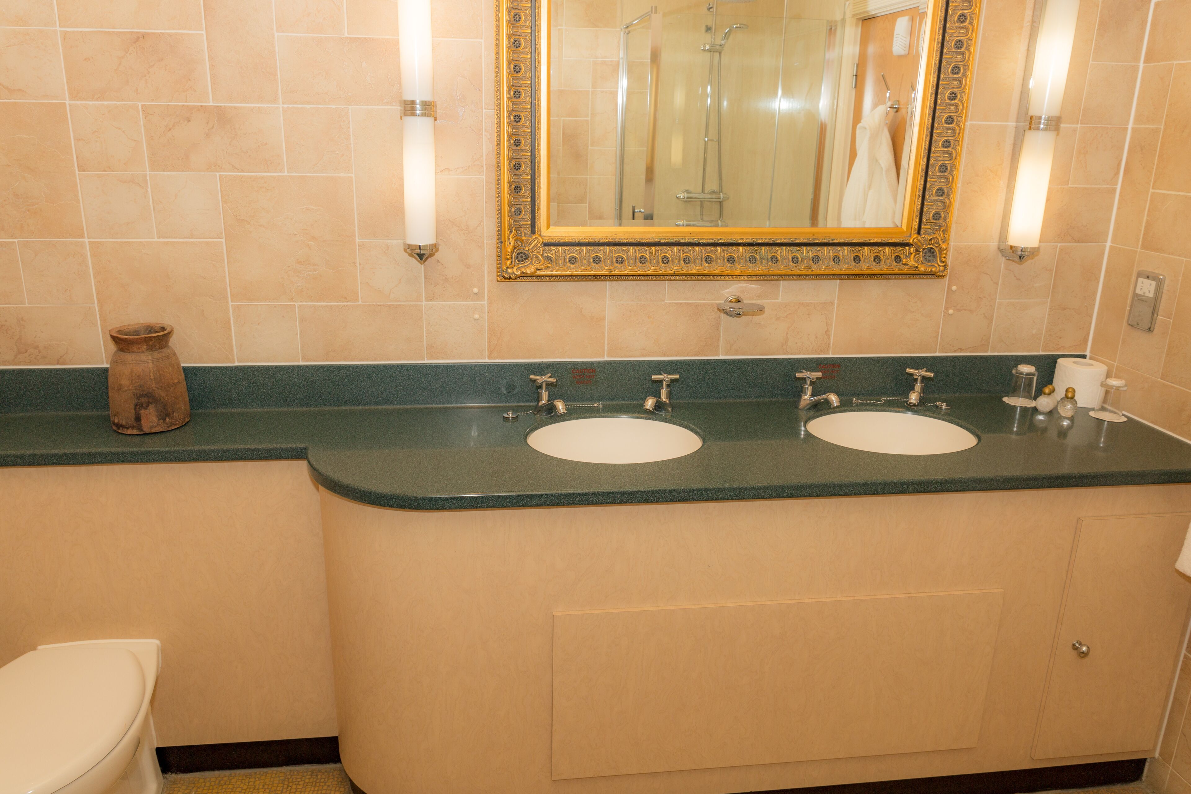 Un baño con dos lavamanos, un inodoro y un espejo con marco decorativo.