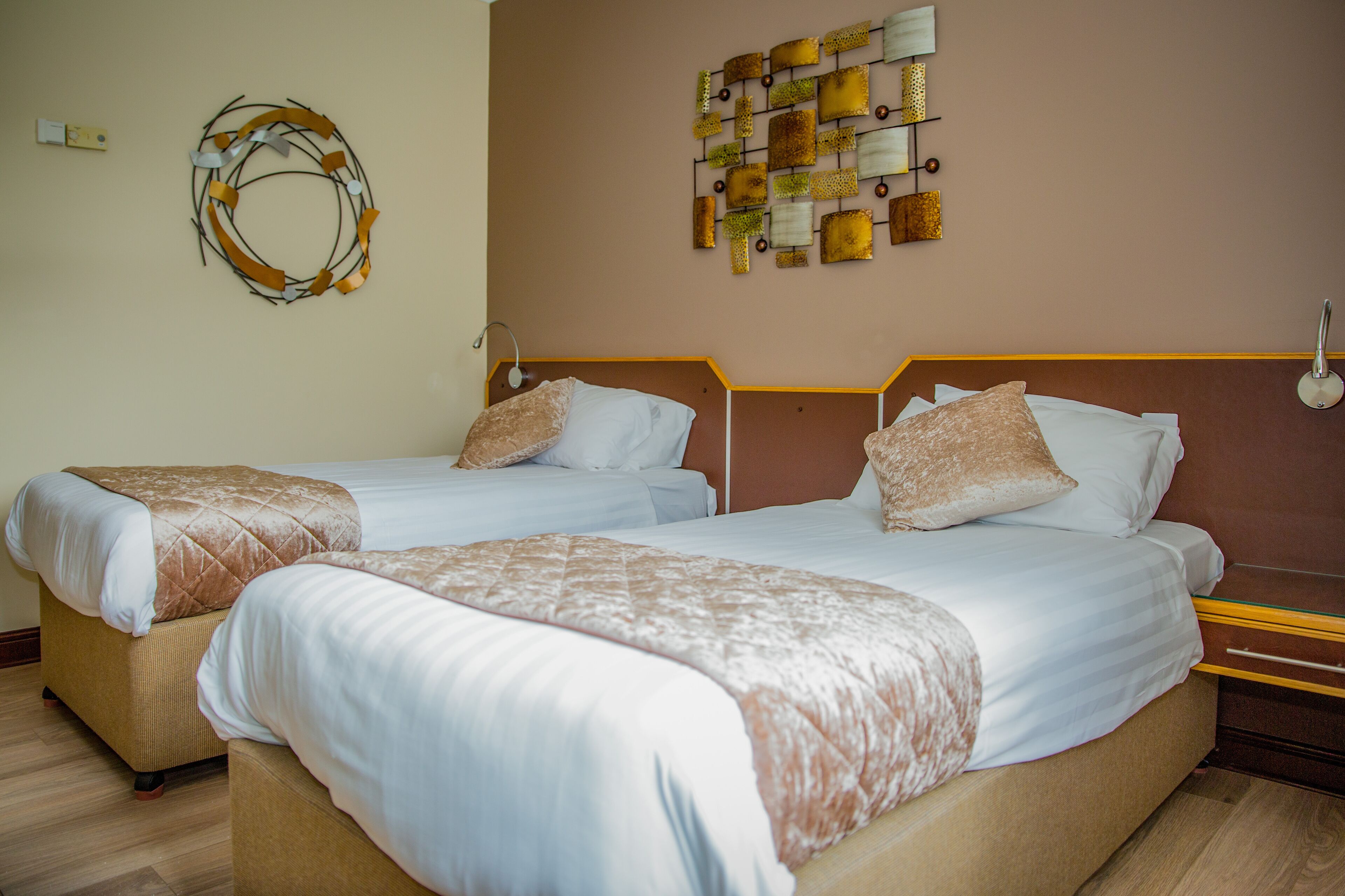 A hotel room with two beds, a wooden headboard, a wall art piece, and a light switch.