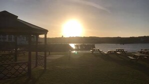 A lakeside setting with a gazebo and picnic tables, a dock extending into the water, and a sunset in the background. - Little Haven Hotel On The Beach (South Shields)