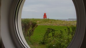 A view through a window of a red lighthouse on a grassy field, with a fence and a wooden structure in the foreground. - Little Haven Hotel On The Beach (South Shields)