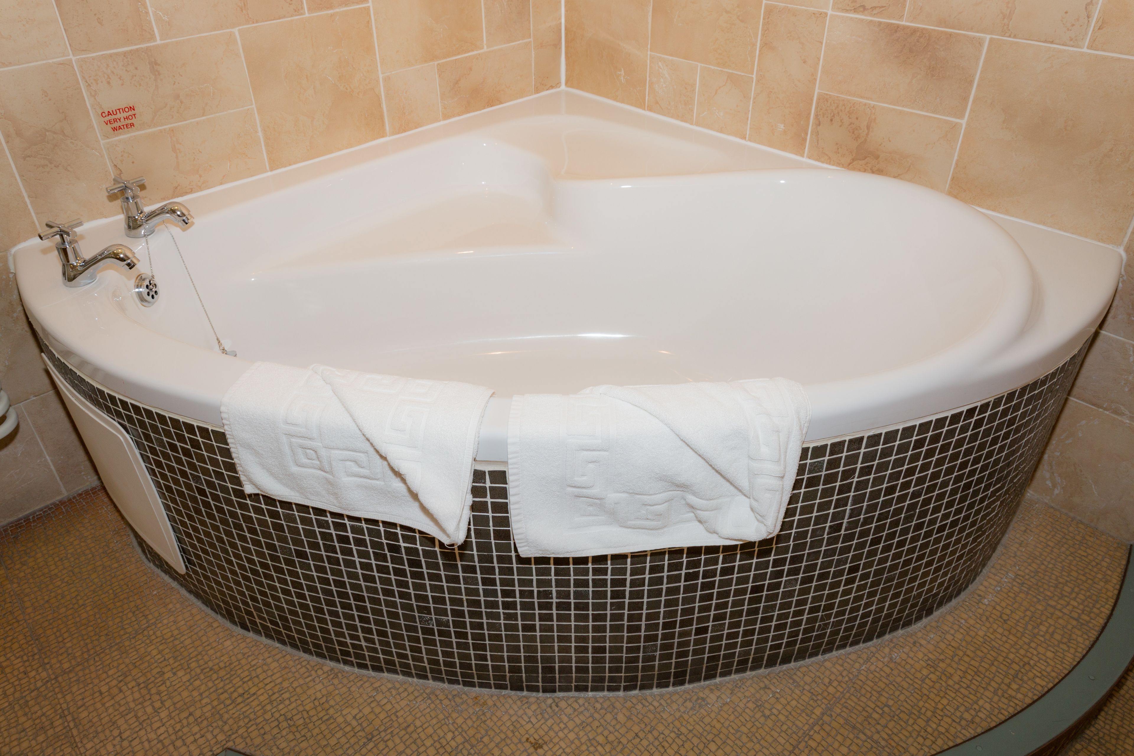 A bathtub with two towels, a faucet, and a tiled wall.