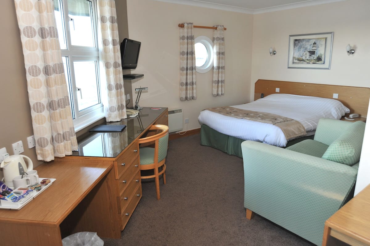 Ein Hotelzimmer mit Bett, Schreibtisch mit Stuhl, Fernseher und einem Fenster mit Vorhängen.