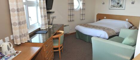 Una habitación de hotel con cama, escritorio con silla, televisión y ventana con cortinas.