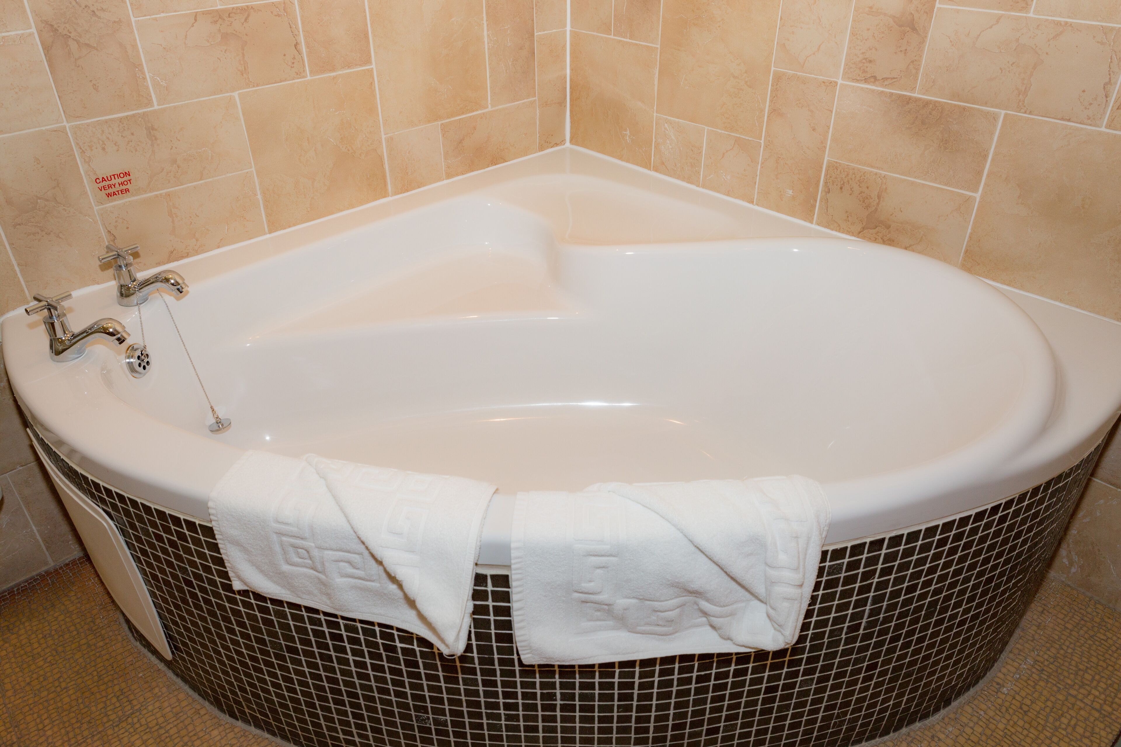 Una bañera grande y ovalada con dos llaves y un desagüe, rodeada de paredes de mosaicos.