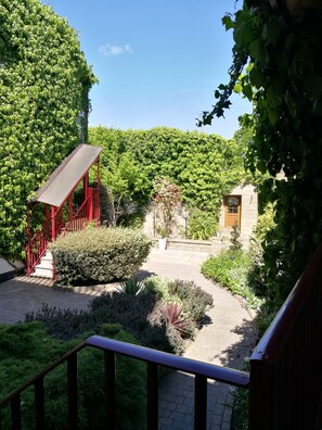 A garden pathway leading to a red structure with a door, surrounded by lush greenery and a stone building. - The Garrison Hotel (Sheffield)