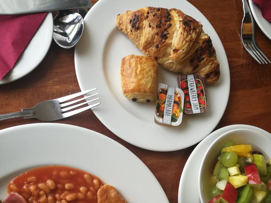 Ein Frühstückstisch mit Speisen, darunter Eier, Bohnen, Pilze, Toast und einem Obstsalat.
