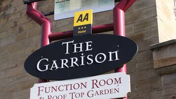 Een hotelschild met verschillende namen, waaronder 'Garrison Hotel', 'The Garrison', 'Function Room & Roof Top Garden' en 'The Jailhouse'.