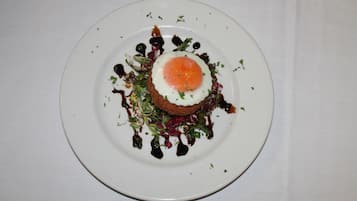 A white plate with a fried egg on top of a bed of greens and a dark sauce.